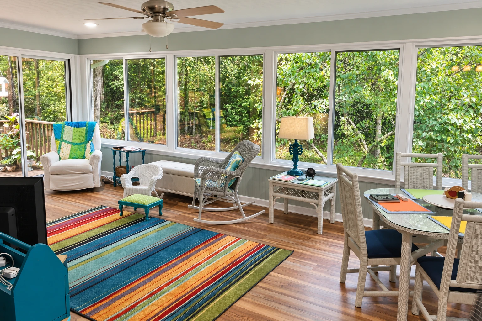 Finished sunroom with broad windows, wood flooring, a striped rug, and seating and dining areas.
