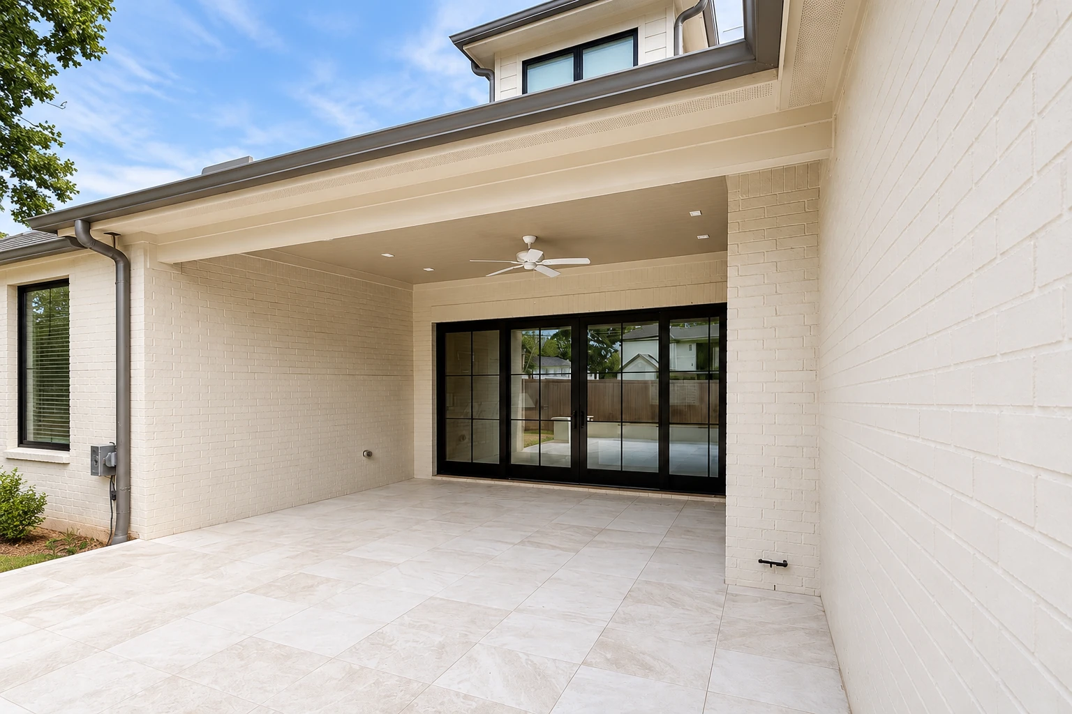 Covered patio with a broad cream roof, tiled floor, ceiling fan, and black-framed sliding glass doors.