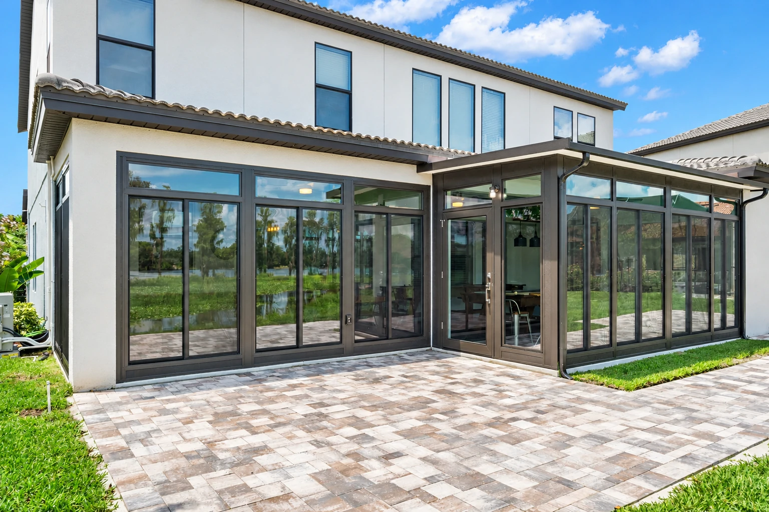 Modern patio enclosure with dark-framed glass panels attached to a white two-story house.