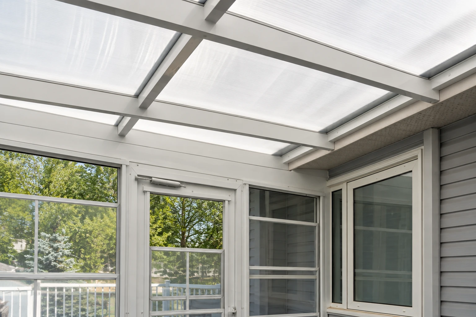 Enclosed patio with a translucent roof, white framing and large screened windows overlooking trees.