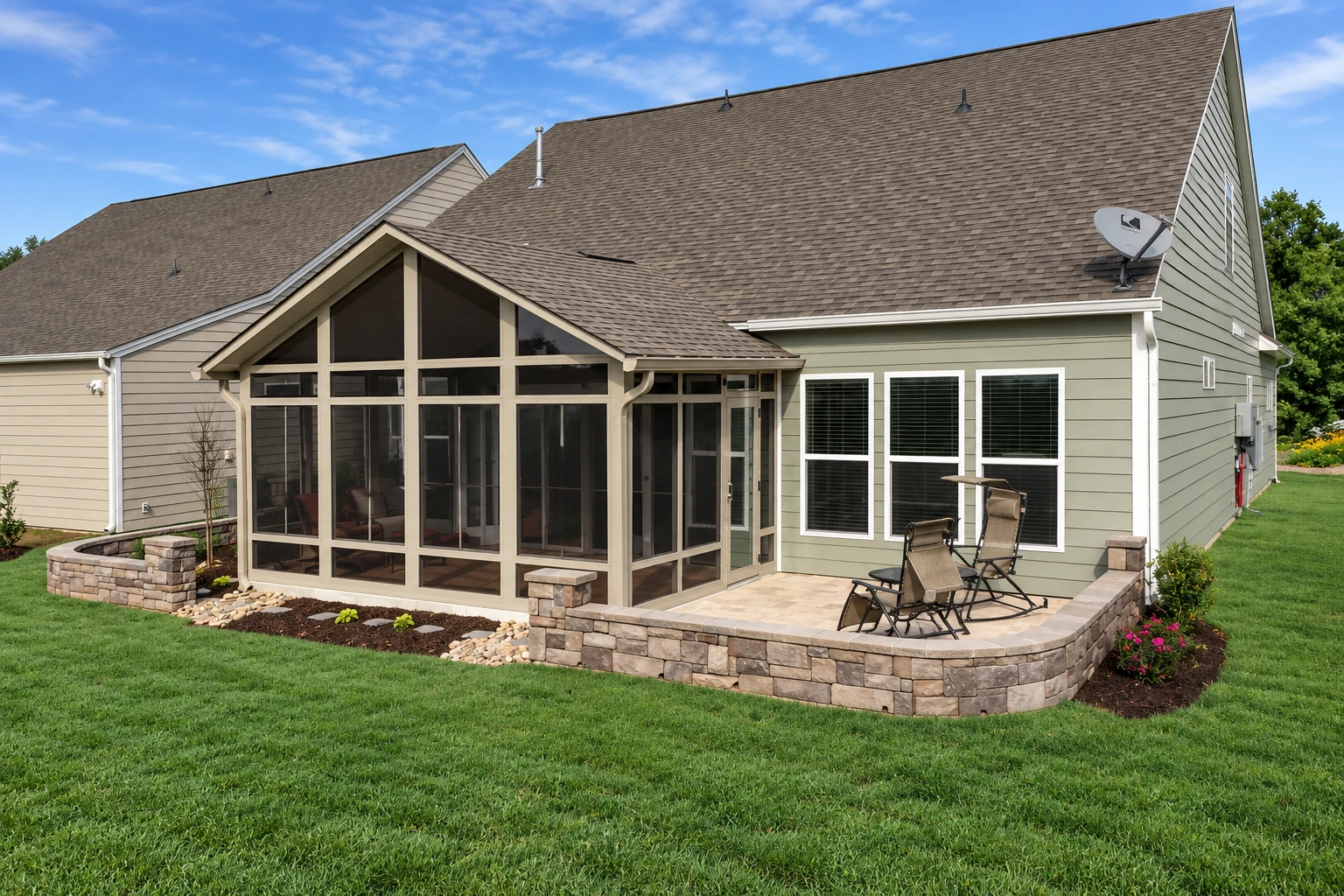 Sunroom addition with a peaked glass front and stone patio beside a gray-green house.