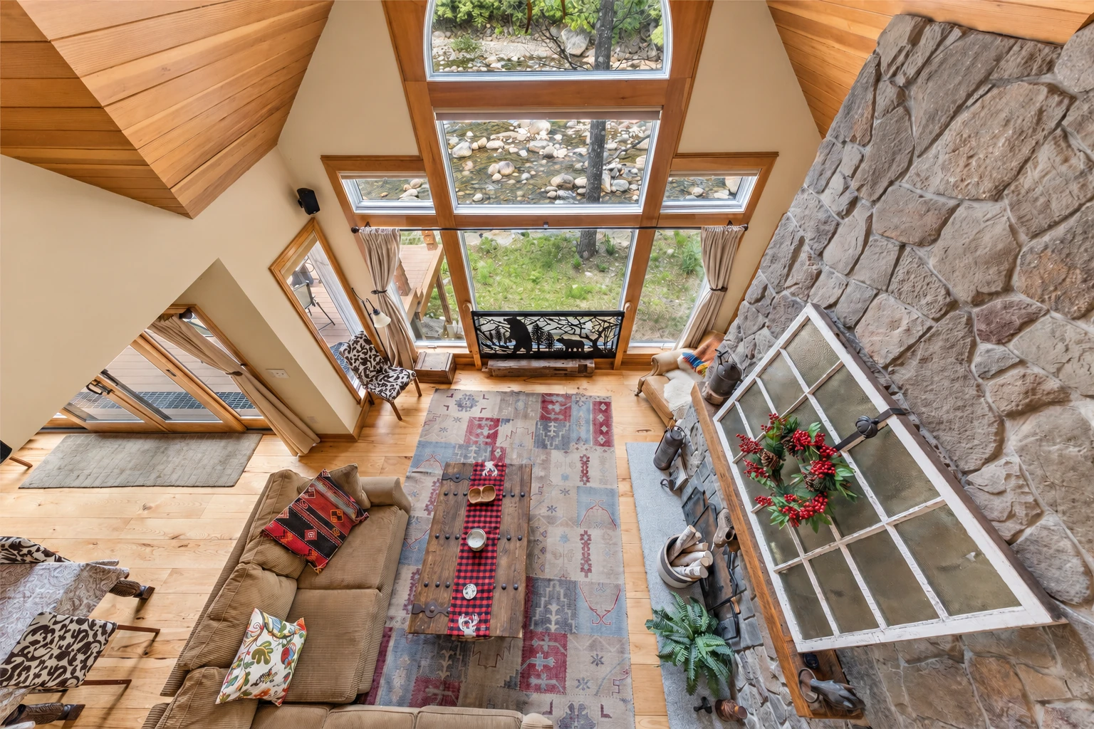 A wood-paneled sunroom viewed from above has skylights, a tall stone fireplace, and a seating area around a rug.