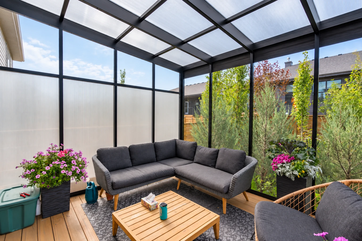 Furnished sunroom with a dark-framed translucent roof, sectional sofa, wood floor and potted flowers.